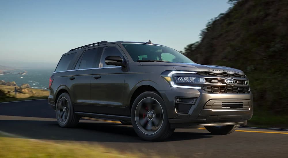A 2022 Ford Expedition Stealth Performance Edition is shown driving on a road with a view of the ocean.