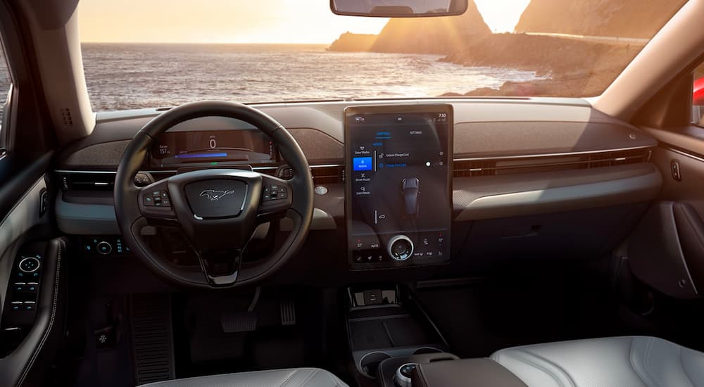 The front dashboard and infotainment screen of a 2022 Ford Mustang Mache-E are shown with an ocean view.