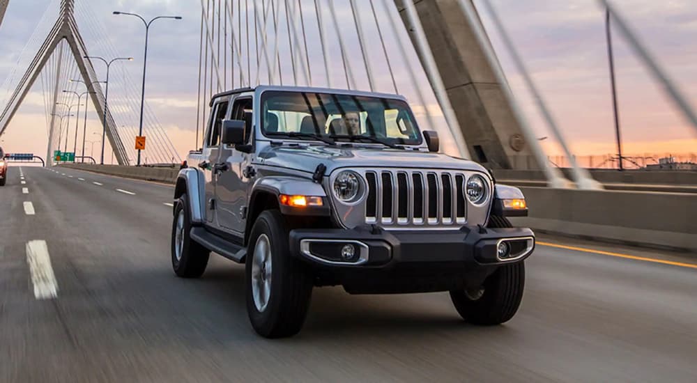 A silver 2021 Jeep Wrangler Unlimited is shown from the front driving on a bridge.