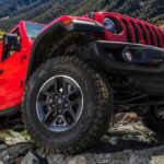 A red 2021 Jeep Wrangler Rubicon Unlimited is shown from the front side driving up a rocky path.