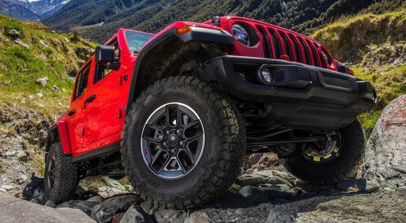 A red 2021 Jeep Wrangler Rubicon Unlimited is shown from the front side driving up a rocky path.