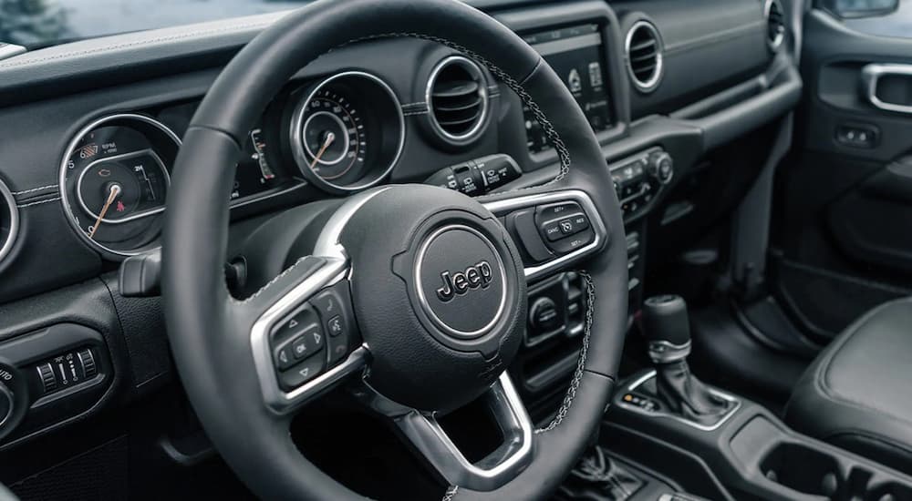 A close up of the silver and black interior of a 2021 Jeep Wrangler shows the steering wheel at a Jeep dealership.