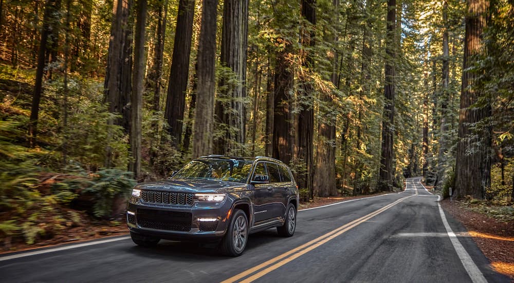 A grey 2022 Jeep Grand Cherokee L Summit Reserve is shown driving through a forest.