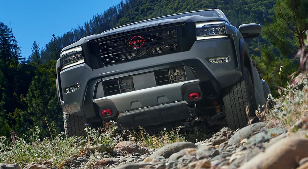 A close up of the front of a grey 2022 Nissan Frontier PRO-4X is shown driving up a rocky path.