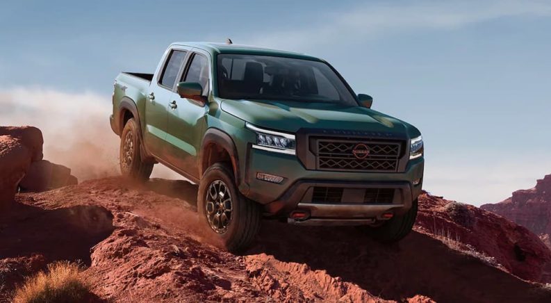 A green 2022 Nissan Frontier PRO-4X is shown driving down a desert road.