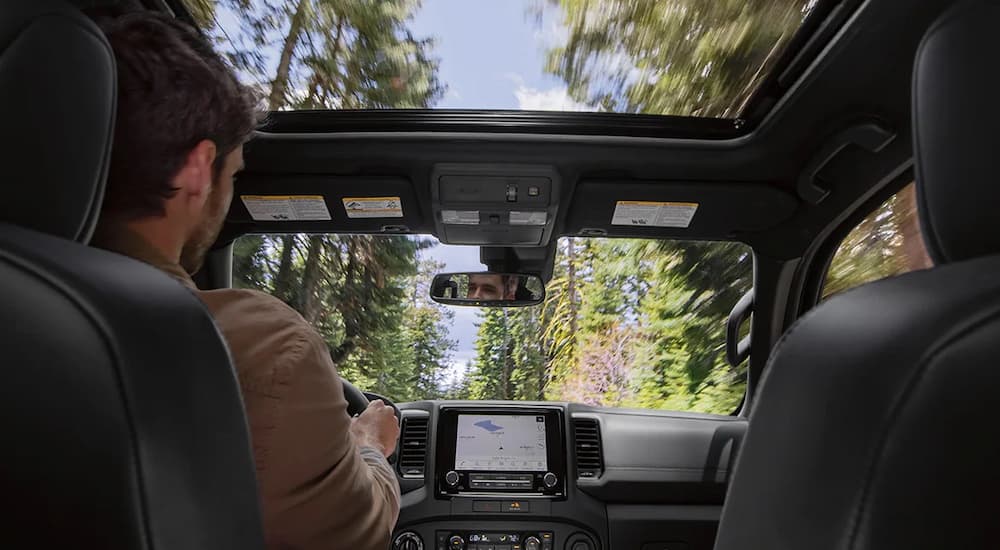 The interior of a 2022 Nissan Frontier is shown as a man drives home from his Nissan Frontier Dealer.