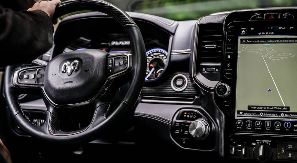 The black interior of a 2021 Ram 1500 shows the steering wheel and infotainment screen.
