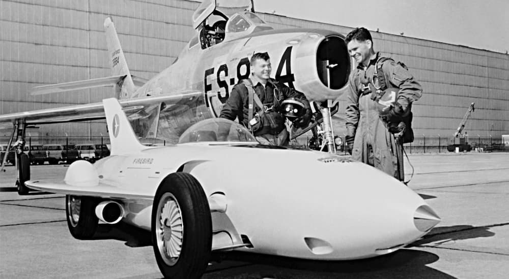 A 1953 GM Firebird 1 is parked next an airplane shown in black and white.