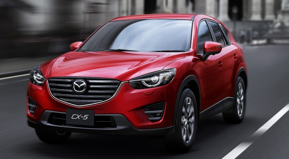 A red 2015 Mazda CX-5 is shown from the front leaving a used car dealer.