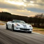 A white 2013 Chevy Corvette 427 60th Anniversary Edition is shown driving down the road on the way to visit a used car lot.