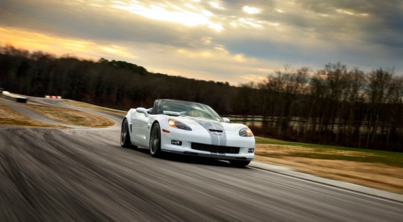 A white 2013 Chevy Corvette 427 60th Anniversary Edition is shown driving down the road on the way to visit a used car lot.