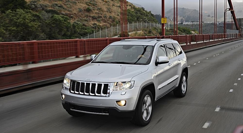 A silver 2011 used Jeep Grand Cherokee is shown driving on a bridge.