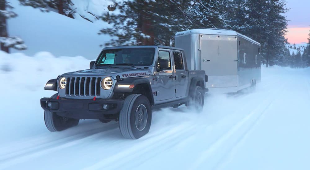 A grey 2020 Jeep Gladiator Sport Rubicon is shown towing a trailer on a snowy road.