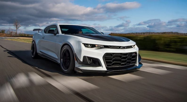 A white 2021 Chevy Camaro ZL1 Coupe is shown driving on a road during a 2021 Chevy Camaro vs 2021 Dodge Challenger comparison.