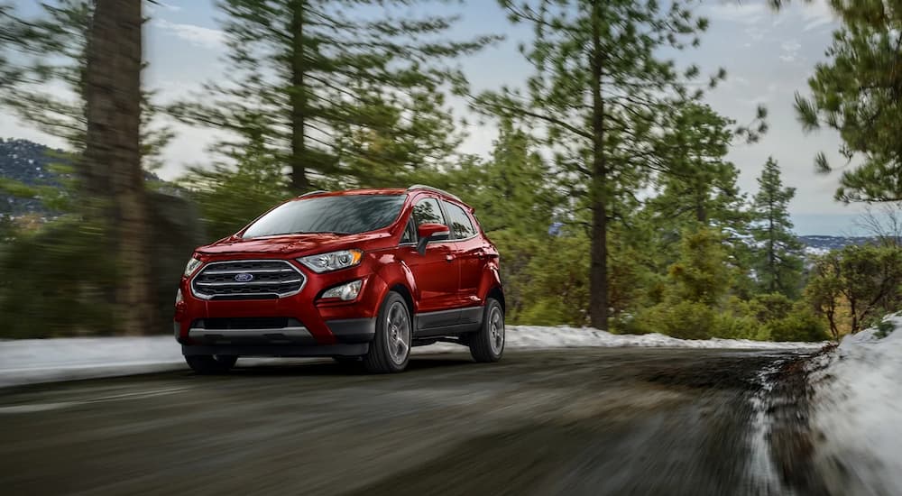 A red 2021 Ford Ecosport is shown driving on a road through a snowy forest.