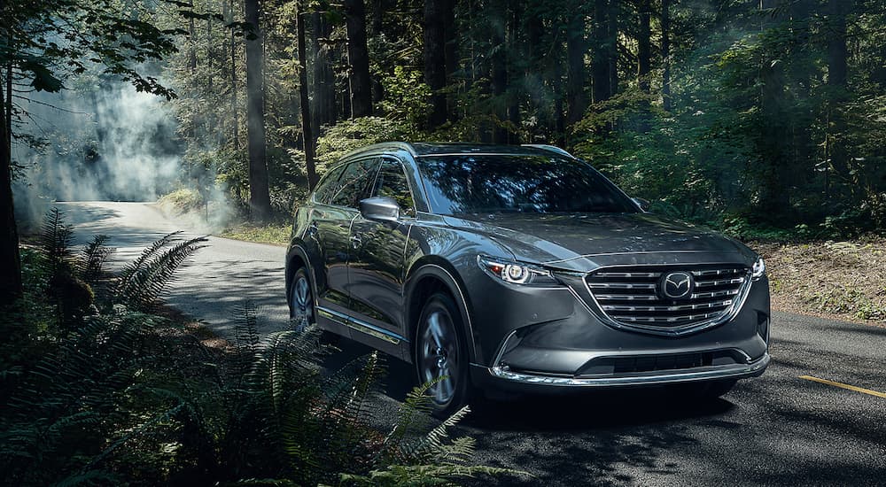 A grey 2021 Mazda CX-9 is shown driving on a road in the woods during a 2021 Ford Explorer vs 2021 Mazda CX-9 comparison.