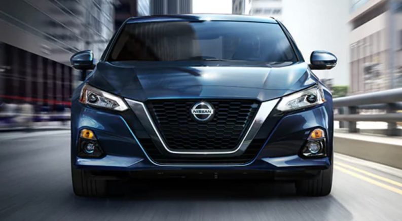 A blue 2021 Nissan Altima is shown from the front driving down a city highway.