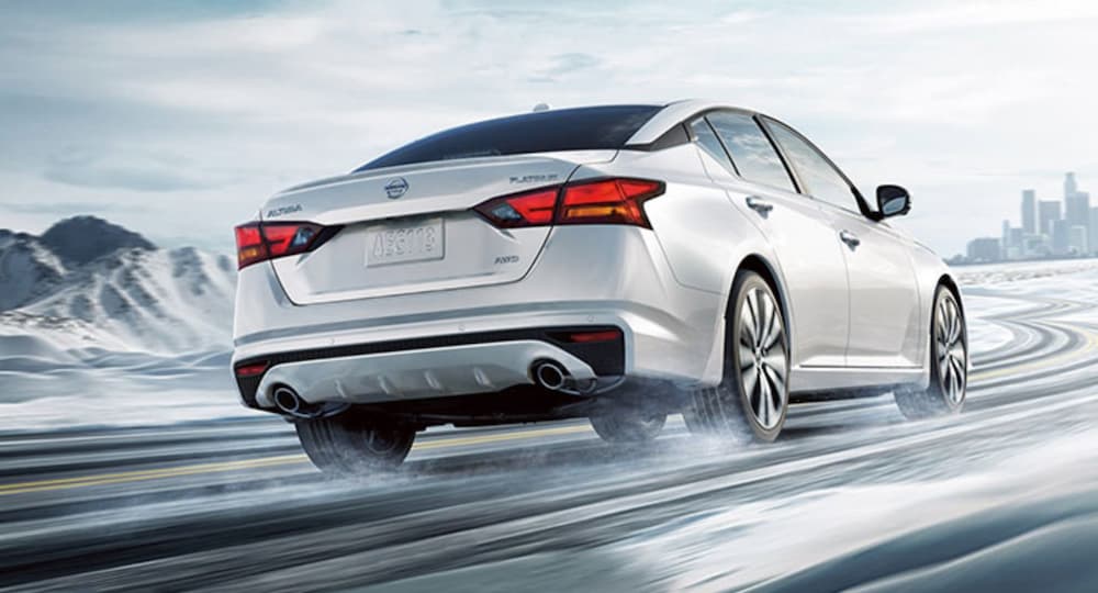 A silver 2021 Nissan Altima is shown from the back as it drives down a snowy road.