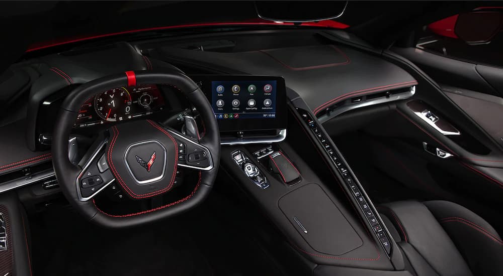 The black and red accent interior of a 2022 Chevy Corvette Stingray shows the steering wheel and infotainment screen.