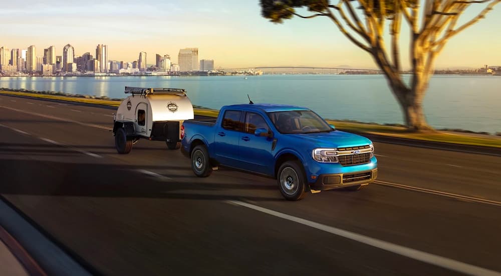 A blue 2022 Ford Maverick XLT is shown towing a small teardrop camper.