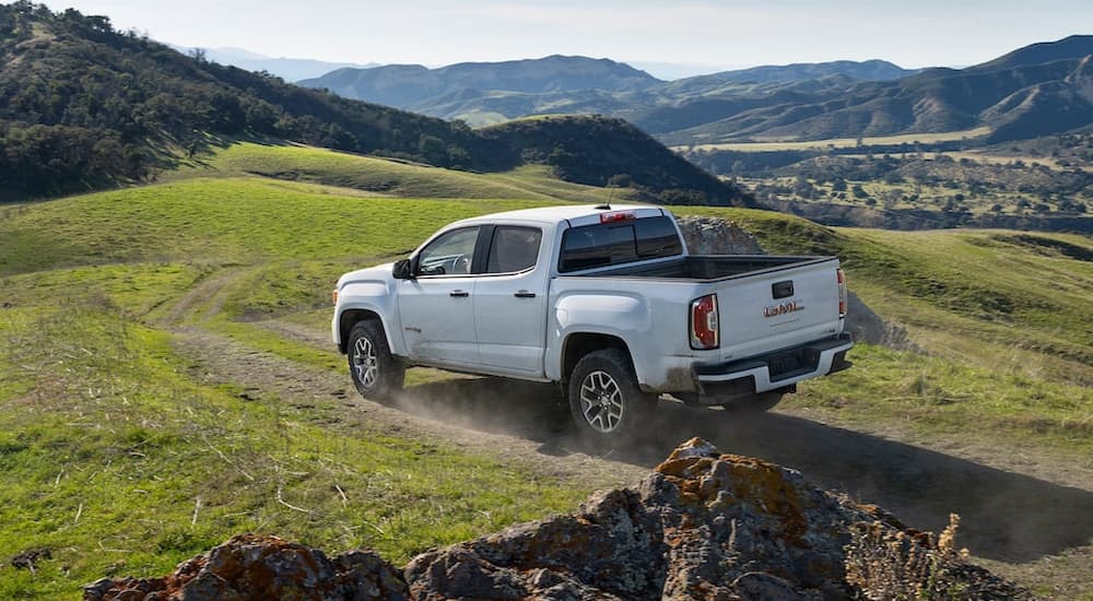 A white 2022 GMC Canyon AT4 is shown from a rear angle driving through a grassy field.