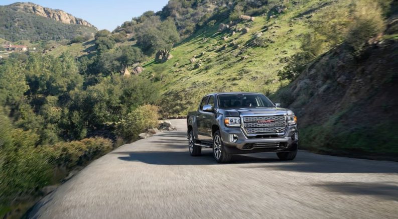 A silver 2022 GMC Canyon is shown driving up a paved road in the mountains.