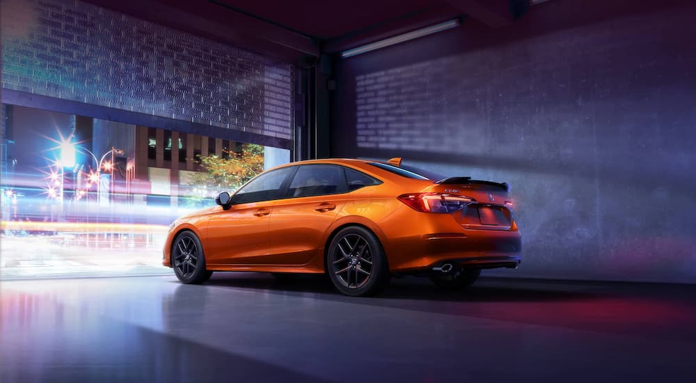 An orange 2022 Honda Civic Si is shown leaving a garage at a Honda dealer.