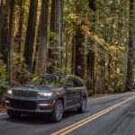 A grey 2022 Jeep Grand Cherokee is shown driving on an empty road in a forest.