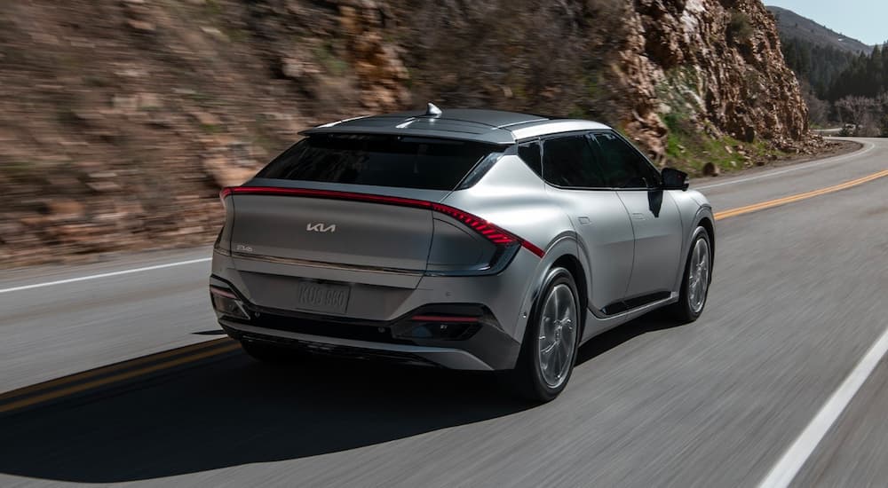A silver 2022 Kia EV6 is shown from the rear driving through the mountains.