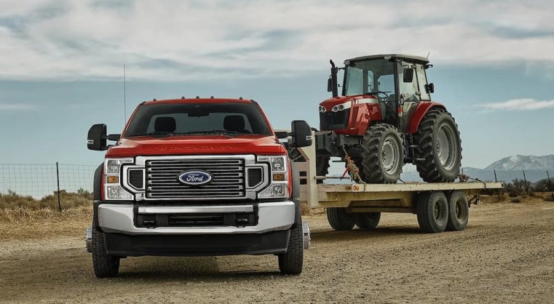 A red 2022 Ford Super Duty XL F-450 is shown towing a red tractor on a trailer.