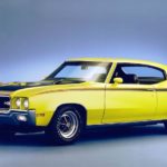 A showgirl is shown standing next to a yellow 1970 Buick GSX at a GM dealer event.