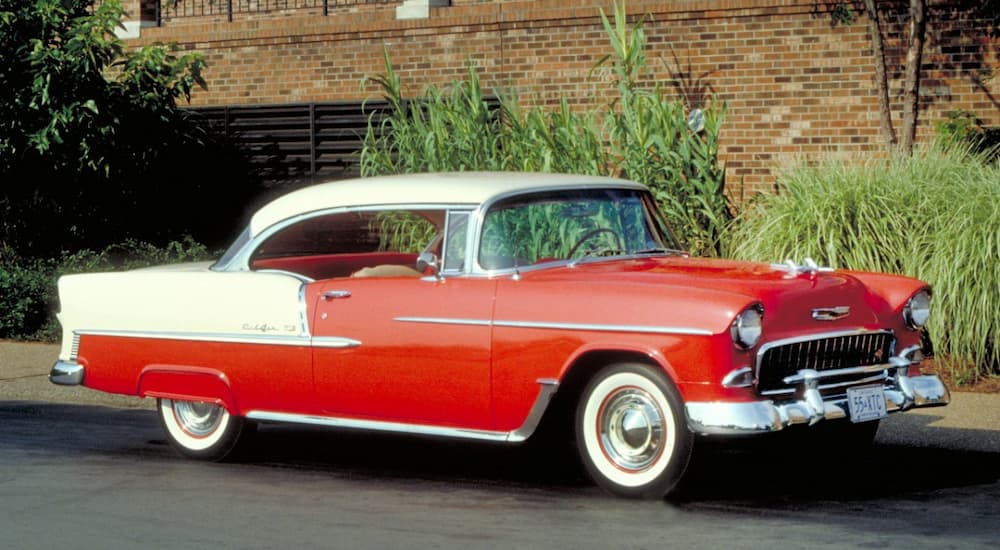 A red 1955 Chevy Bel Air Sport Coupe is shown parked outside of a GM dealer.