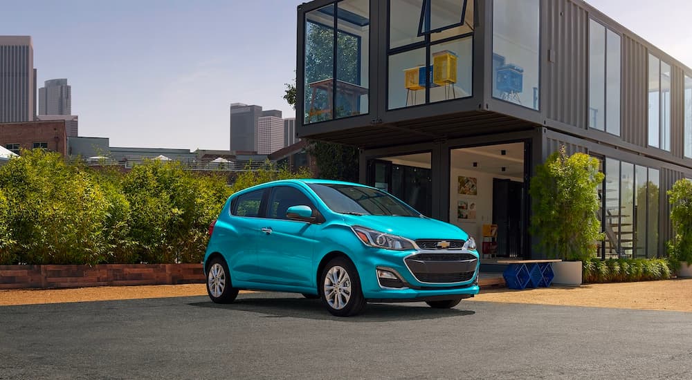 A blue 2022 Chevy Spark is shown parked in front of a modern house.