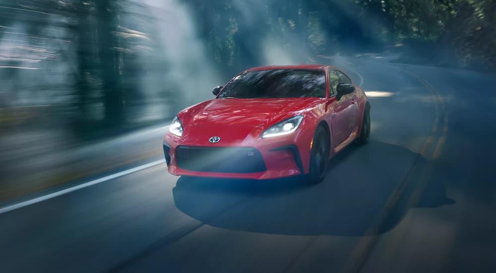 A red 2022 Toyota GR 86 is shown driving through a forest after visiting a Toyota 86 dealership.