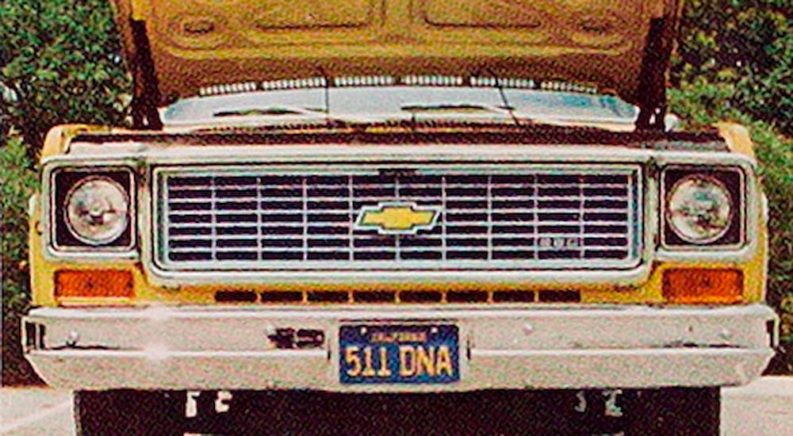 A close up of a yellow 1973 Chevy C-10 shows the grille, headlights, and open hood.