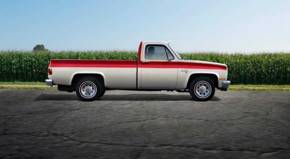 A red and silver 1974 Chevy C-10 is shown from the side at a used truck dealership.