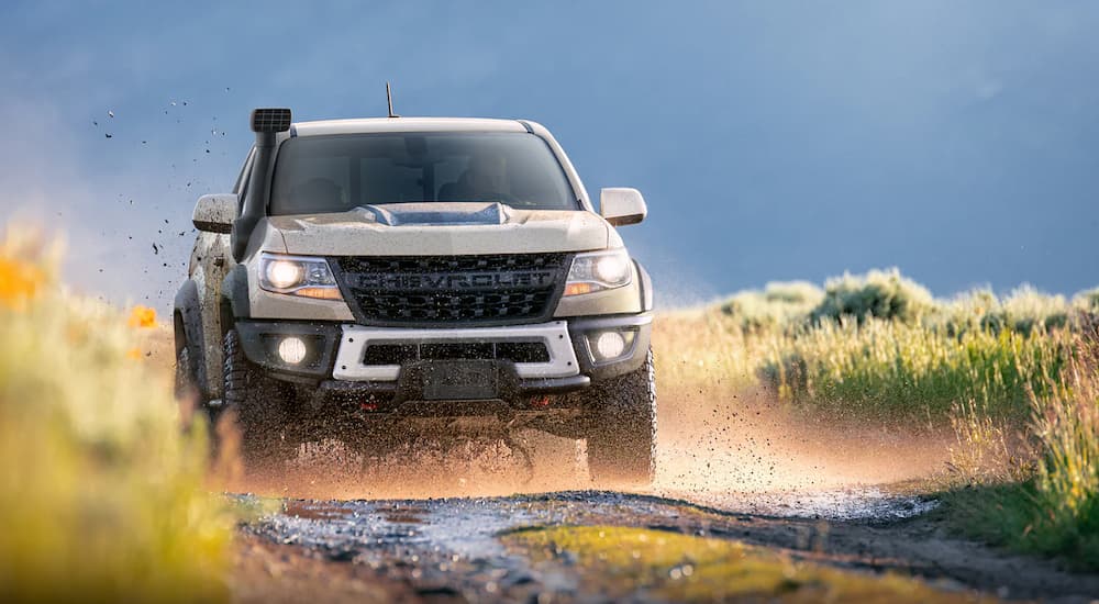 A tan 2021 Chevy Colorado ZR2 is shown driving on a muddy road through a field.