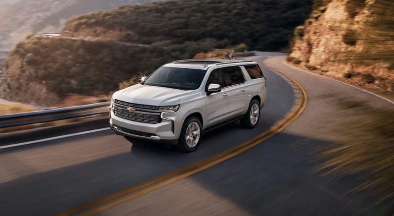 A silver 2022 Chevy Suburban LT is shown driving on a highway through the mountains.