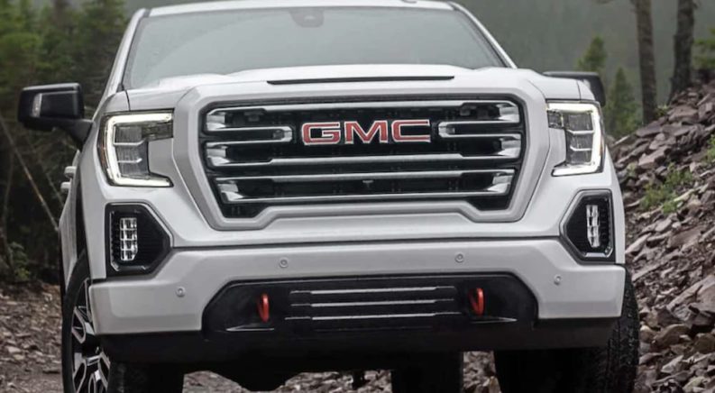 A white 2022 GMC Sierra 1500 is shown from the front off-roading in the mountains after winning a 2022 GMC Sierra 1500 vs 2022 Ram 1500 comparison.