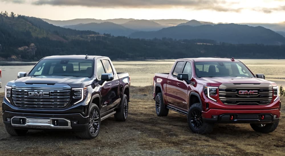 A black 2022 GMC Sierra 1500 Denali Ultimate and a red AT4-X are shown parked in front of a body of water.