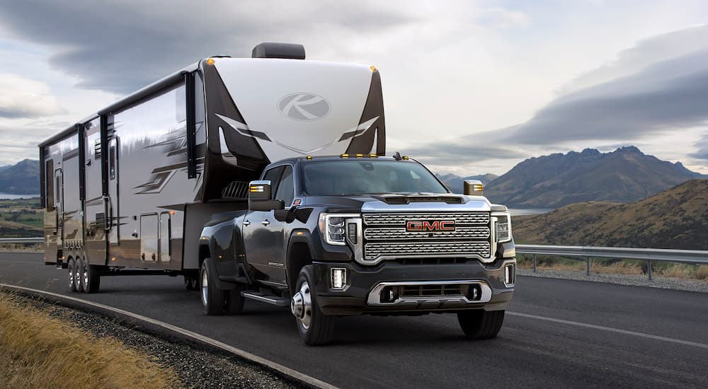 A black 2022 GMC Sierra 3500HD is shown towing a camper on a highway.