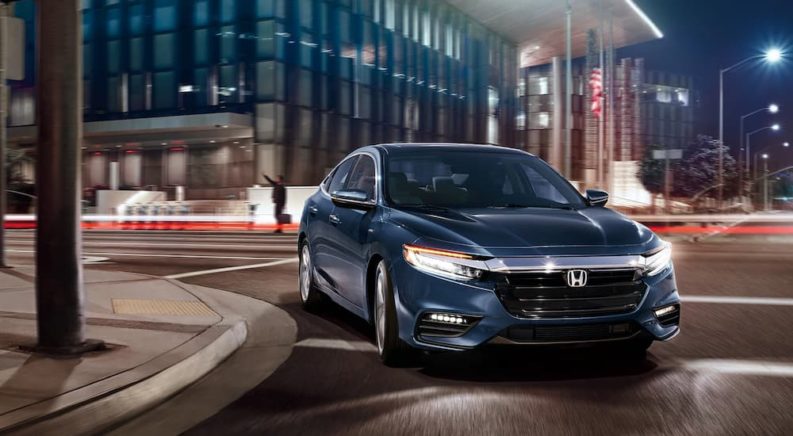A blue 2022 Honda Insight Touring is shown driving around a corner in a city.