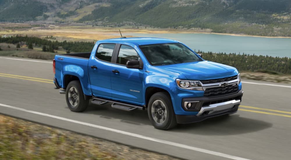 A blue 2022 Chevy Colorado is shown from the side driving on an open road past a body of water.