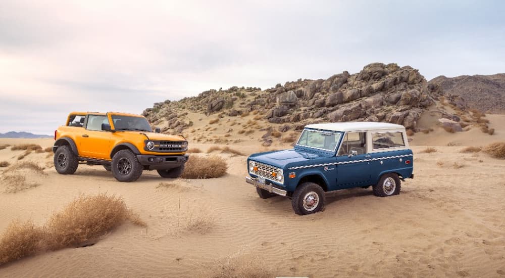 A blue 1st generation Ford Bronco and yellow 2021 Ford Bronco are shown in a desert.