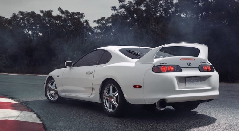 A white 1994 Toyota Supra is shown from behind parked on a racetrack after visiting a used vehicle dealership.