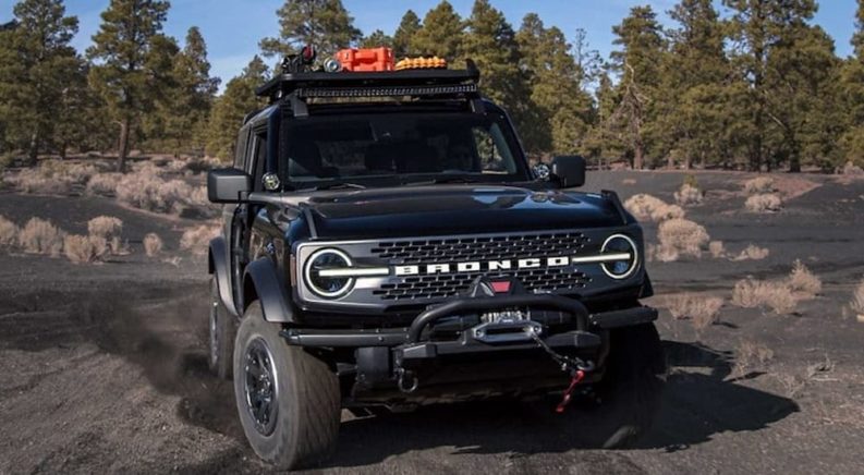 A black 2021 Ford Bronco WildTrak is shown off-roading on a rocky trail.
