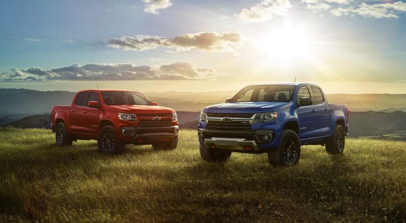 A red and a blue 2022 Chevy Colorado Trail Boss are shown from the front while parked in grass.