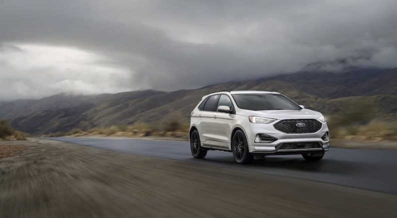 A silver 2022 Ford Edge is shown driving down an empty road.
