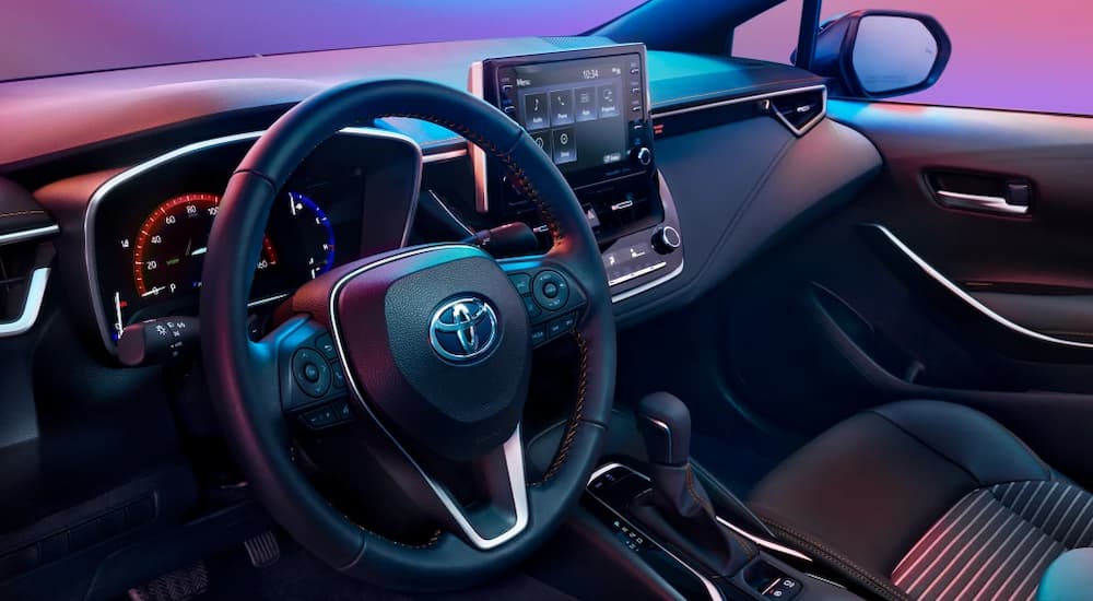 The black and silver accented interior of a 2022 Toyota Corolla shows the steering wheel and infotainment screen.