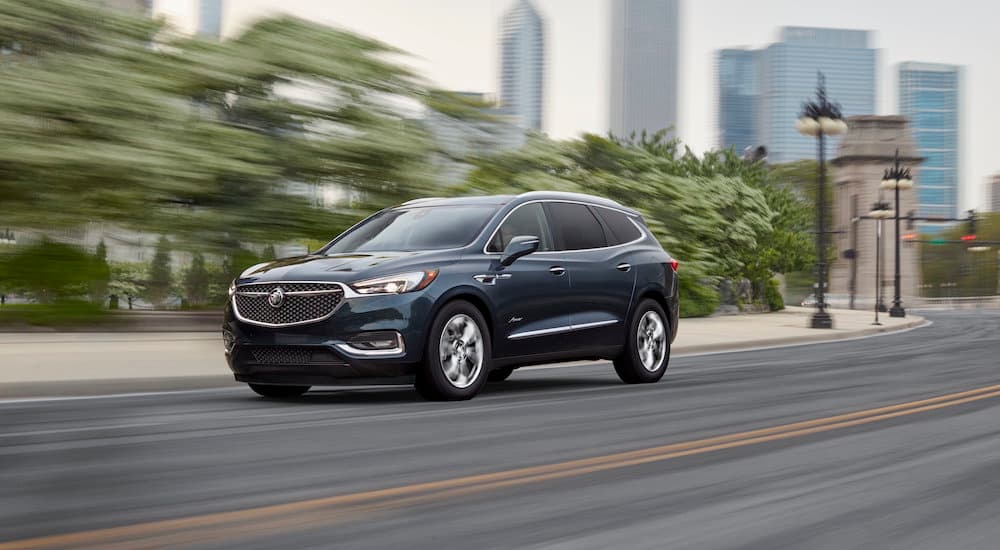 A dark blue 2018 Buick Enclave Avenir is shown driving on a city street after leaving a Buick dealer.